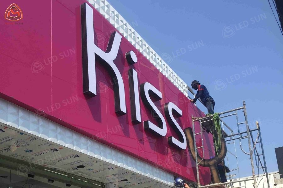 Thợ lắp bảng hiệu chữ nổi “Kiss” trên mặt tiền màu hồng